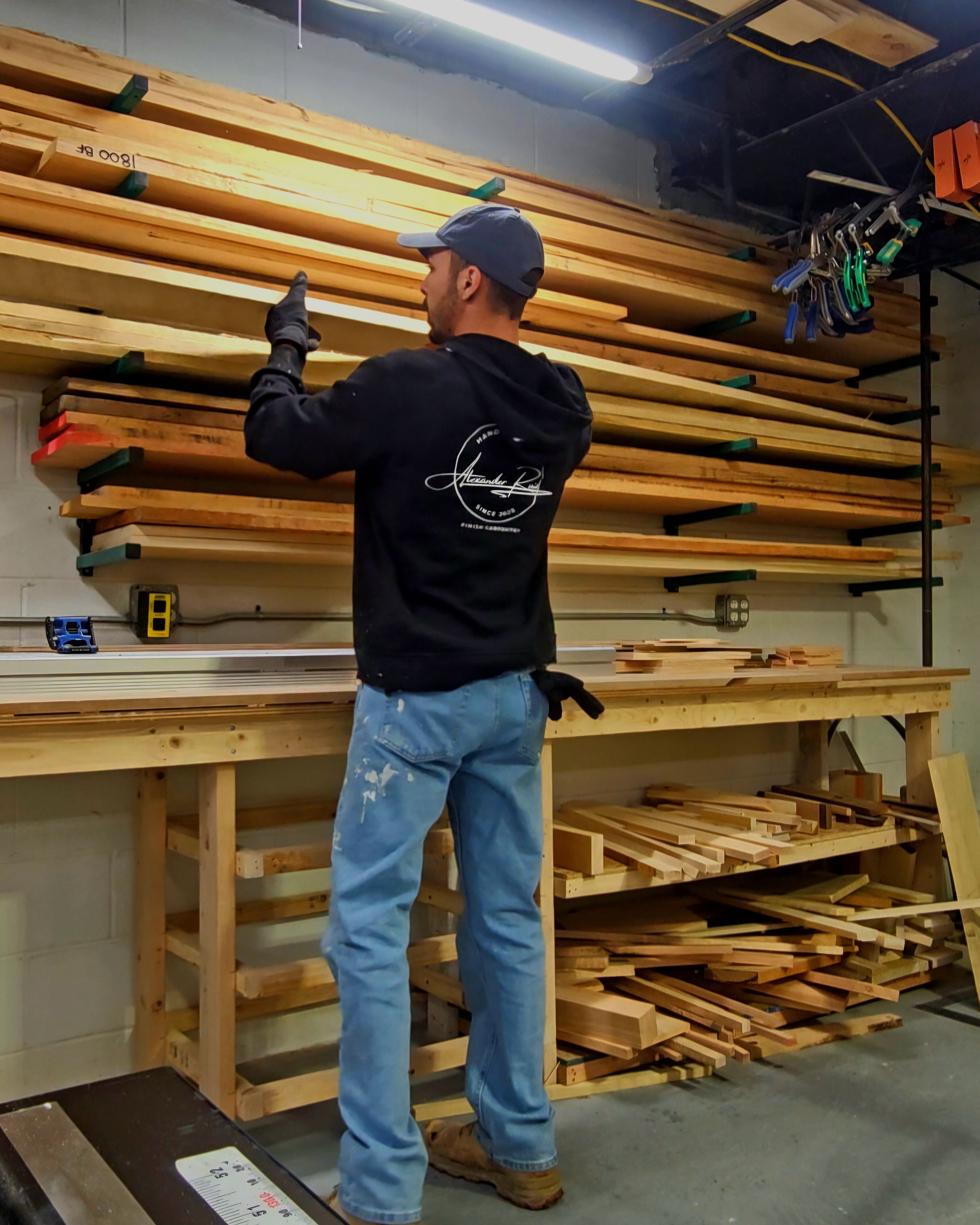 Person working with wooden planks in a workshop setting. Custom furniture maker.
